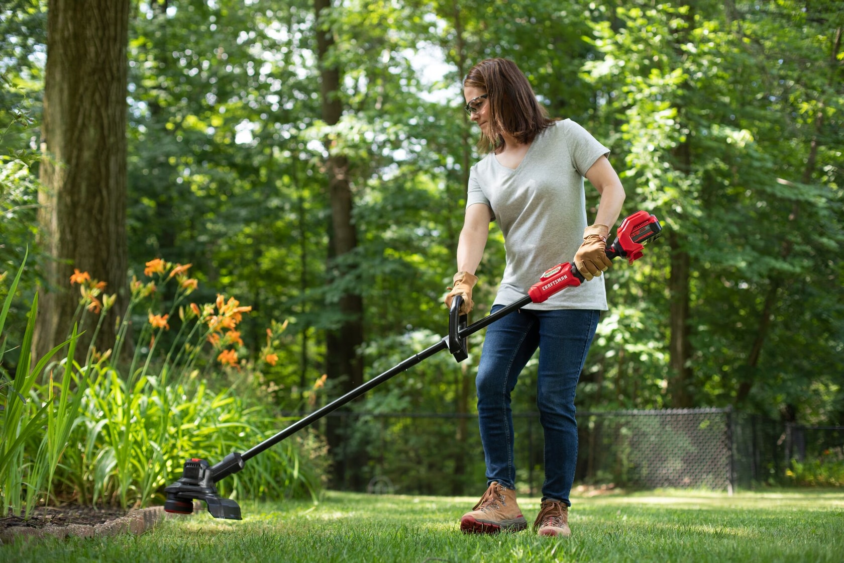 CRAFTSMAN V20 BRUSHLES PR String Trimmer trimming around flowerbed with trees in background