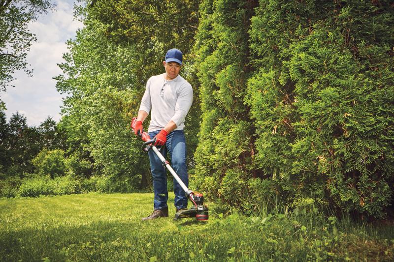 20 volt cordless 13 inch weedwacker string trimmer edger with push button feed being used by a person to trim grass outdoors.