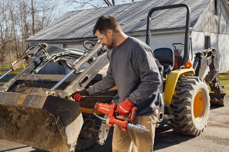 Photo of end-user applying grease with grease gun to farm equipment.