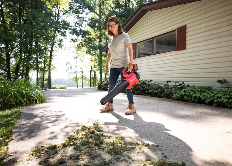 CRAFTSMAN V20 BRUSHLESSRP Blower clearing grass off driveway home in background