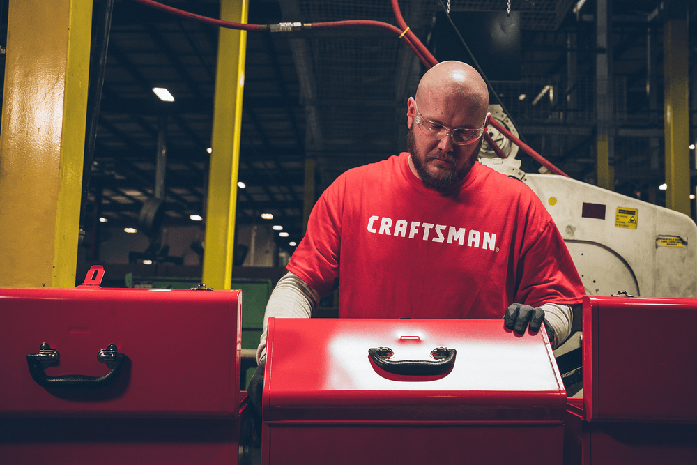 Man in a red CRAFTSMAN t-shirt in a CRAFTSMAN factory inspecting a red CRAFTSMAN tool box.